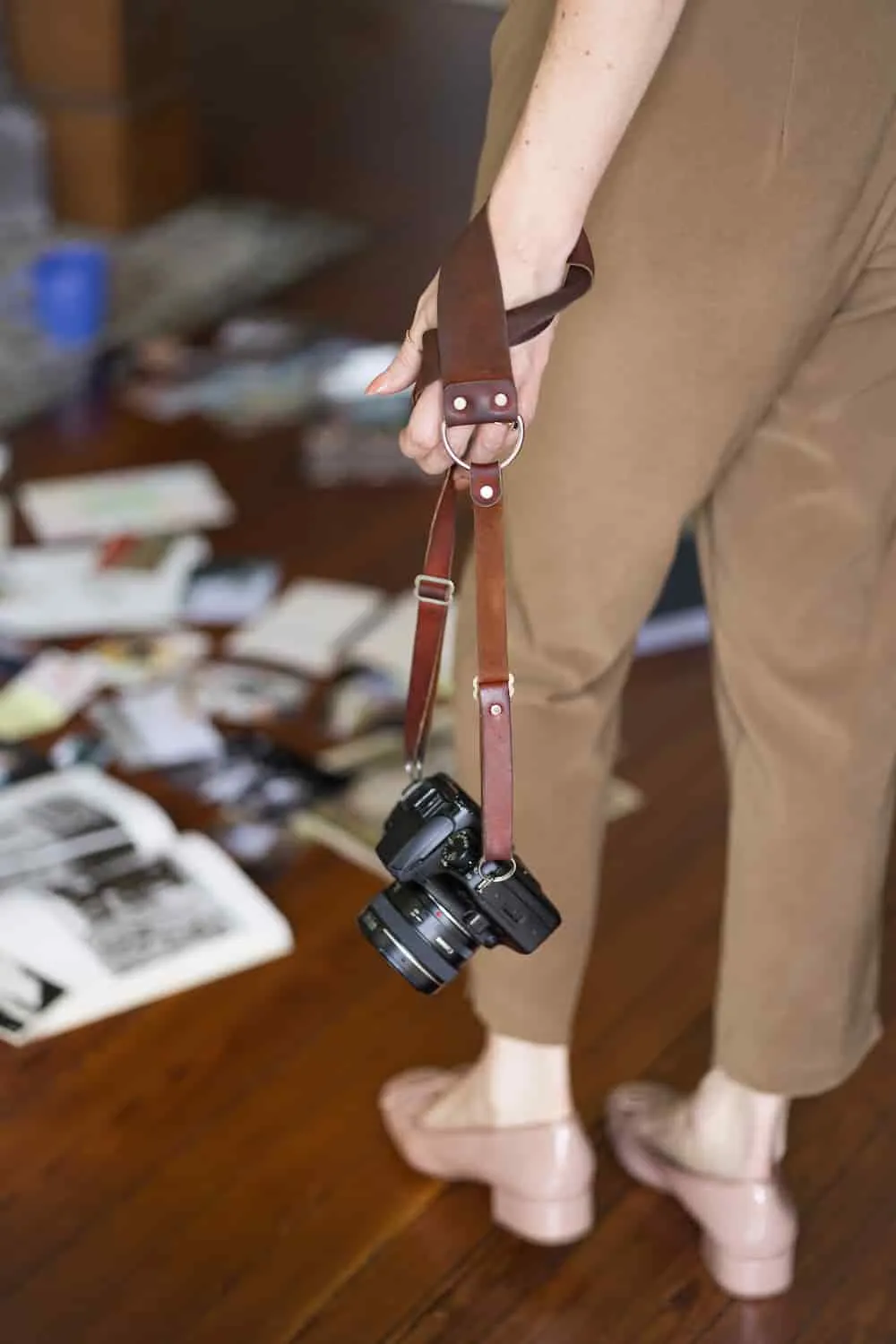 Kendall, holding her 35mm film camera  by the strap looking down at a collection of old phootos